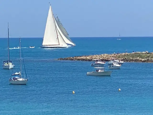 Voilier à grande voile blanche devant les bateaux au mouillage