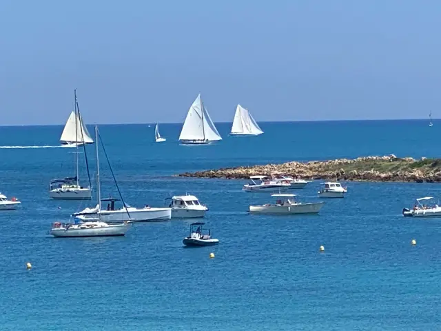 Plusieurs voiliers blancs au large des rochers et des bateaux au mouillage