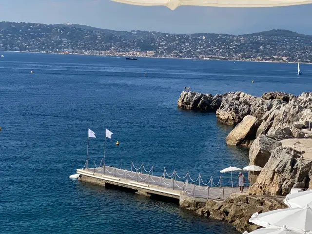 Petit ponton blanc au pied des rochers face à une baie bleue