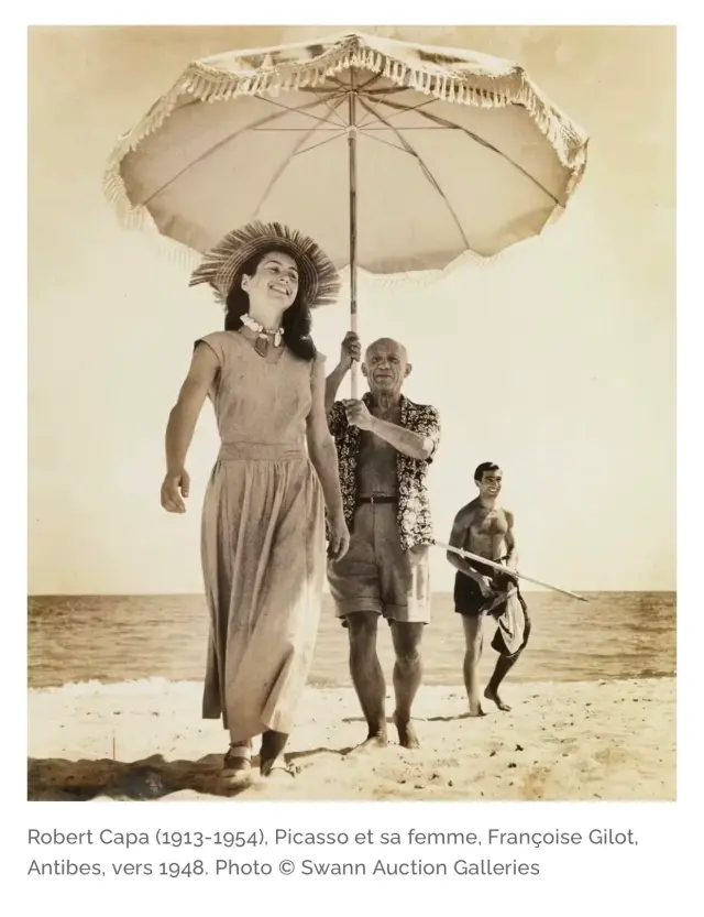 Photographie ancienne de promeneurs sur la plage sous une grande ombrelle